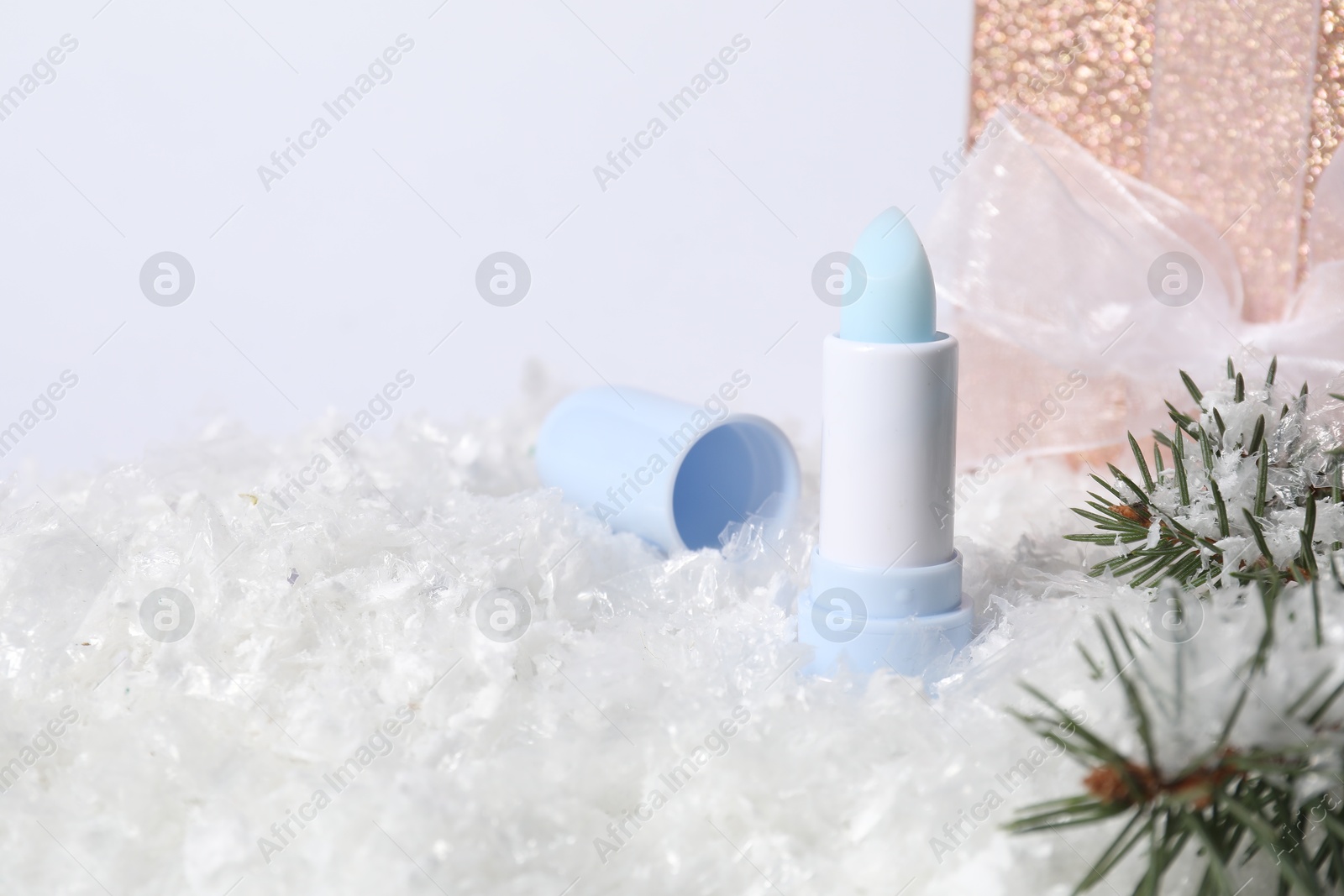 Moisturizing lip balm, gift box and fir tree branches on artificial snow, closeup. Space for text Photo of Moisturizing lip balm, gift box and fir tree branches on artificial snow, closeup. Space for text