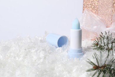 Photo of Moisturizing lip balm, gift box and fir tree branches on artificial snow, closeup. Space for text