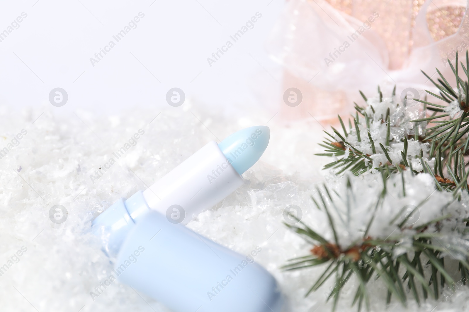 Moisturizing lip balm, gift box and fir tree branches on artificial snow, closeup. Winter care Photo of Moisturizing lip balm, gift box and fir tree branches on artificial snow, closeup. Winter care