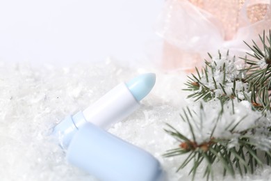 Photo of Moisturizing lip balm, gift box and fir tree branches on artificial snow, closeup. Winter care