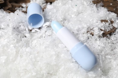 Photo of Moisturizing lip balm on artificial snow, closeup. Winter care
