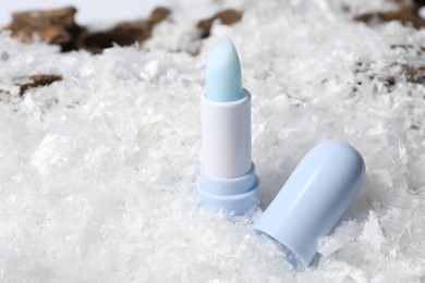 Photo of Moisturizing lip balm on artificial snow, closeup. Winter care
