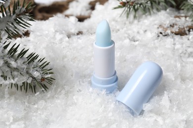 Photo of Moisturizing lip balm and fir tree branches on artificial snow, closeup. Winter care