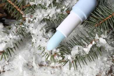 Photo of Moisturizing lip balm and fir tree branches on artificial snow, closeup. Winter care