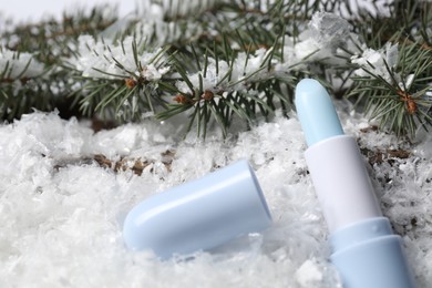 Photo of Moisturizing lip balm and fir tree branches on artificial snow, closeup. Winter care