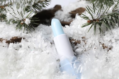 Photo of Moisturizing lip balm and fir tree branches on artificial snow, closeup. Winter care