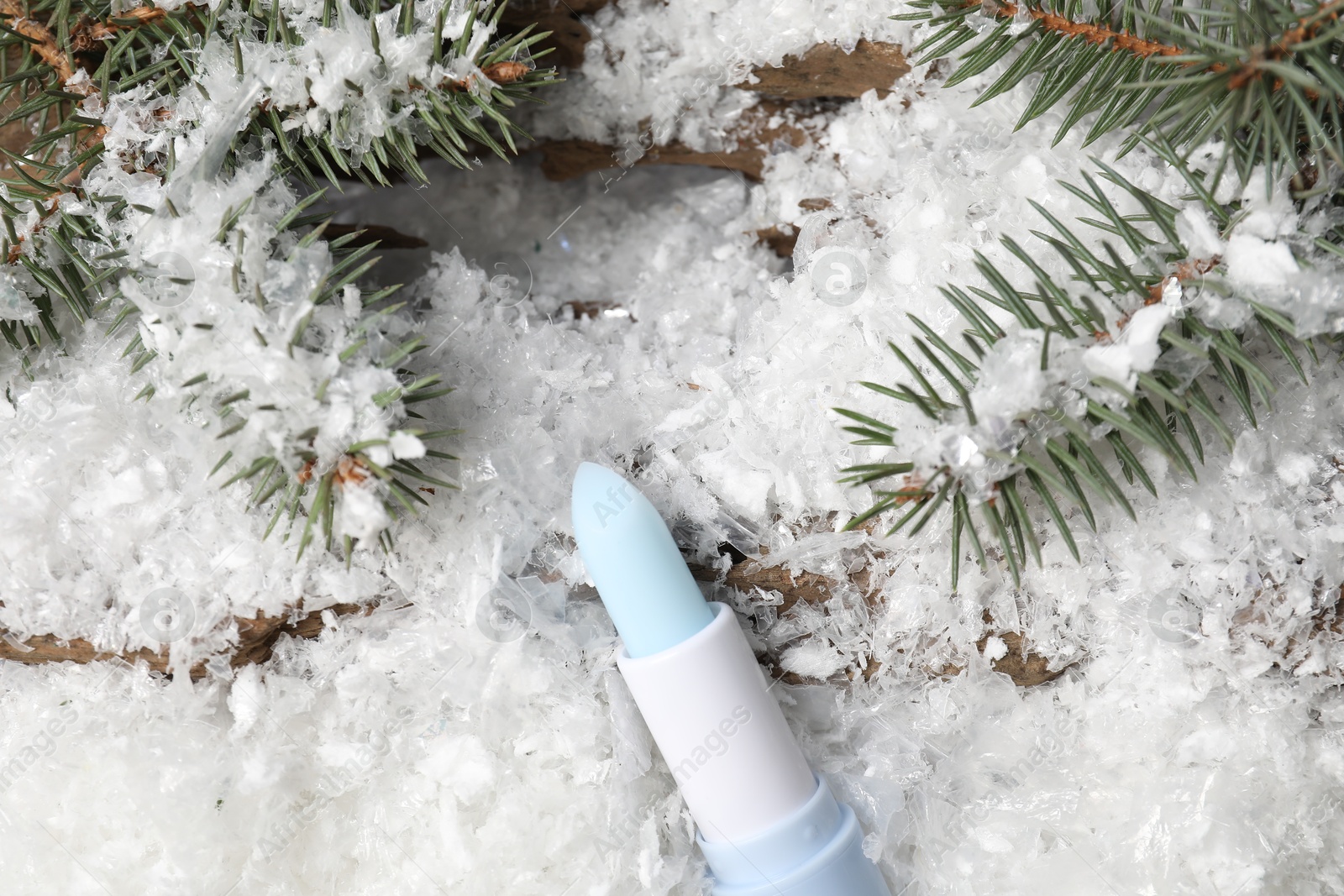 Moisturizing lip balm and fir tree branches on artificial snow, flat lay. Winter care Photo of Moisturizing lip balm and fir tree branches on artificial snow, flat lay. Winter care