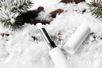 Photo of Moisturizing lip balm and fir tree branches on artificial snow, closeup. Winter care