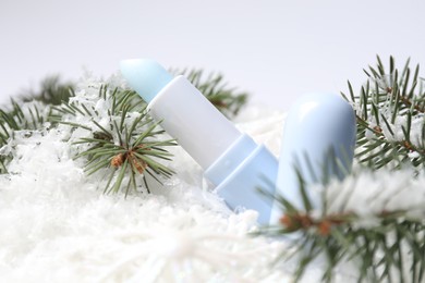 Photo of Moisturizing lip balm and fir tree branches on artificial snow, closeup. Winter care