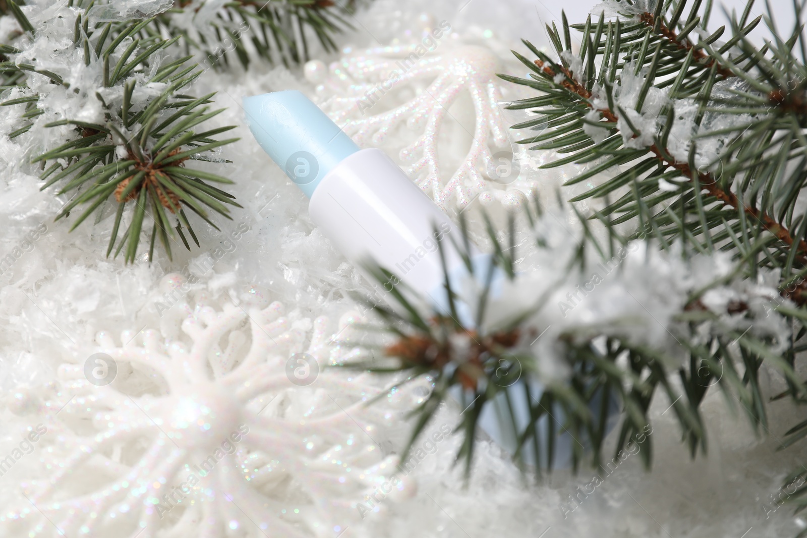 Photo of Moisturizing lip balm, Christmas decor and fir tree branches on artificial snow, closeup. Winter care