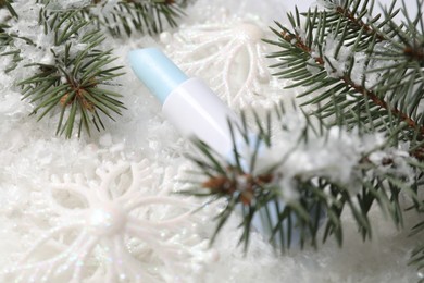 Photo of Moisturizing lip balm, Christmas decor and fir tree branches on artificial snow, closeup. Winter care