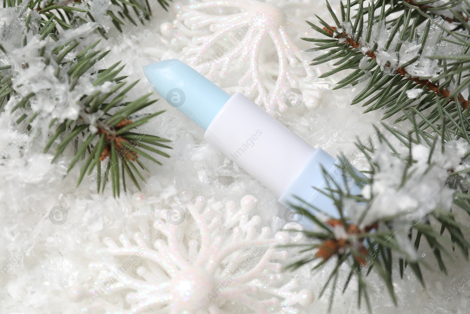 Photo of Moisturizing lip balm, Christmas decor and fir tree branches on artificial snow, closeup. Winter care