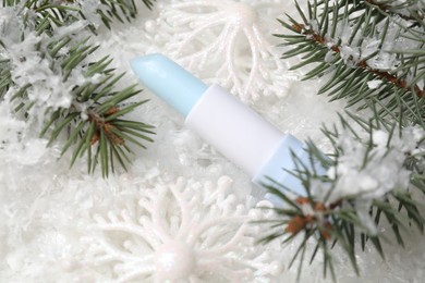 Photo of Moisturizing lip balm, Christmas decor and fir tree branches on artificial snow, closeup. Winter care