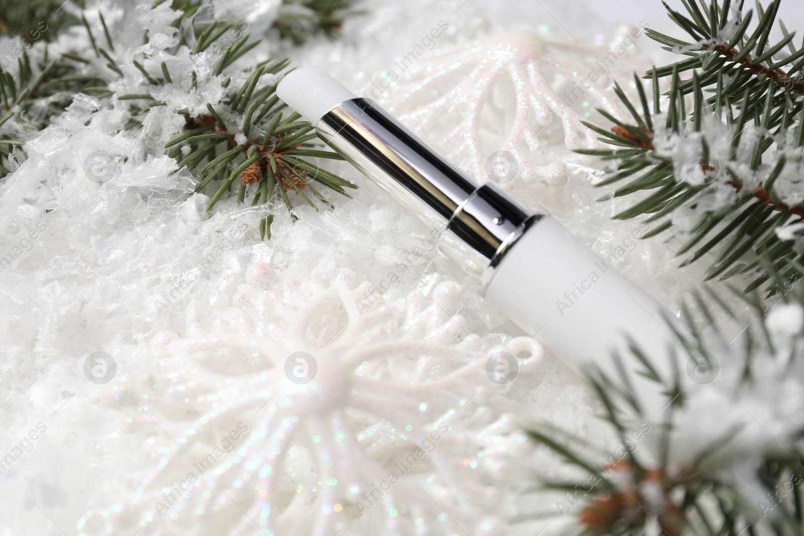 Photo of Moisturizing lip balm, Christmas decor and fir tree branches on artificial snow, closeup. Winter care