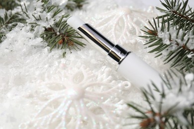 Photo of Moisturizing lip balm, Christmas decor and fir tree branches on artificial snow, closeup. Winter care