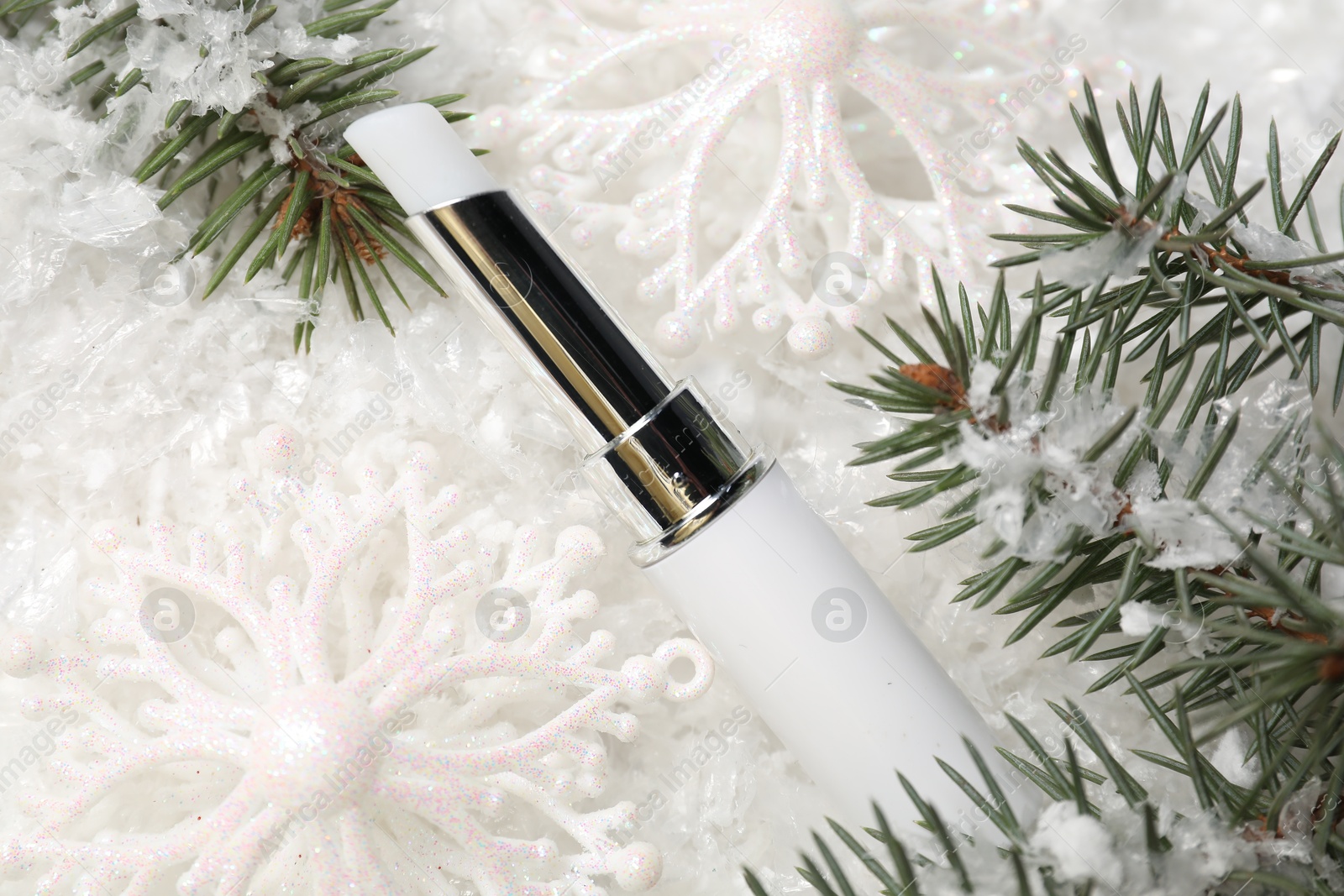 Photo of Moisturizing lip balm, Christmas decor and fir tree branches on artificial snow, closeup. Winter care