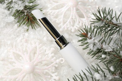 Photo of Moisturizing lip balm, Christmas decor and fir tree branches on artificial snow, closeup. Winter care