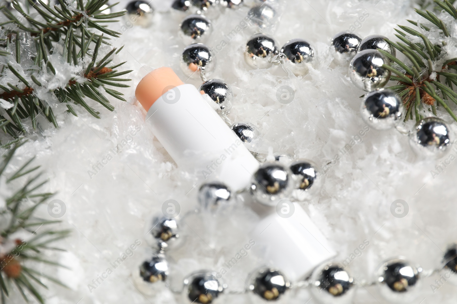 Moisturizing lip balm, Christmas decor and fir tree branches on artificial snow, closeup. Winter care Photo of Moisturizing lip balm, Christmas decor and fir tree branches on artificial snow, closeup. Winter care