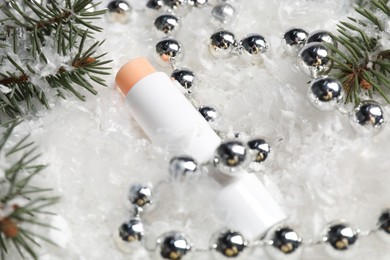 Photo of Moisturizing lip balm, Christmas decor and fir tree branches on artificial snow, closeup. Winter care