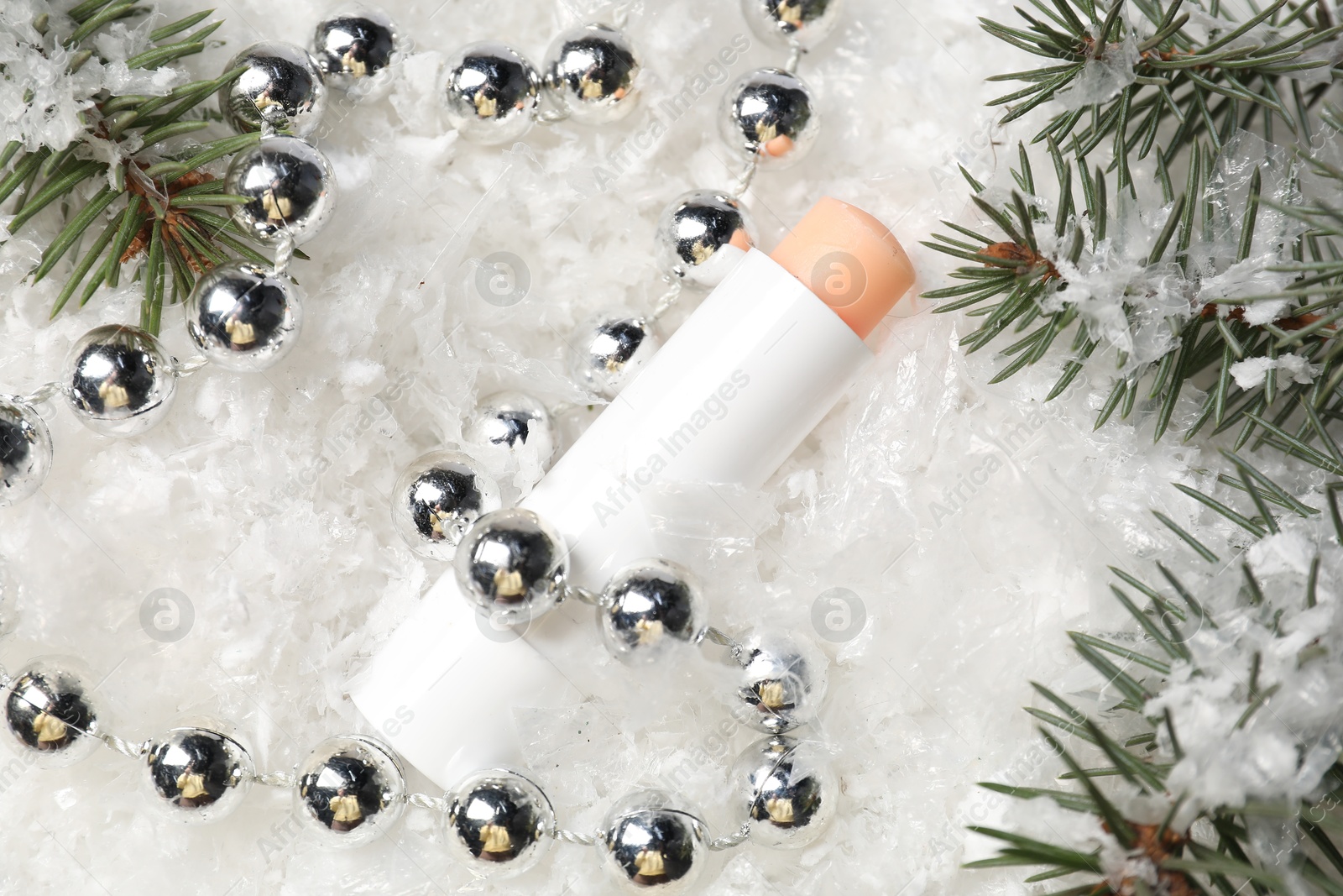 Photo of Moisturizing lip balm, Christmas decor and fir tree branches on artificial snow, flat lay. Winter care