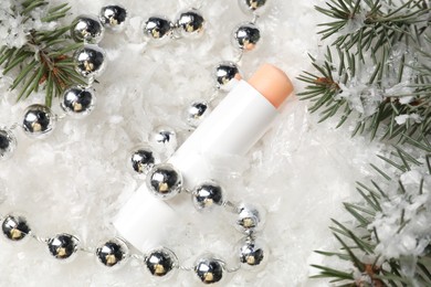 Photo of Moisturizing lip balm, Christmas decor and fir tree branches on artificial snow, flat lay. Winter care