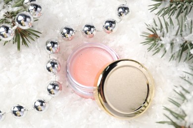 Photo of Moisturizing lip balm, Christmas decor and fir tree branches on artificial snow, closeup. Winter care