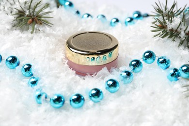 Photo of Moisturizing lip balm, Christmas decor and fir tree branches on artificial snow, closeup. Winter care