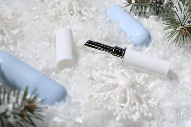 Photo of Moisturizing lip balms, Christmas decor and fir tree branches on artificial snow, closeup. Winter care