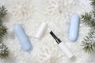 Photo of Moisturizing lip balms, Christmas decor and fir tree branches on artificial snow, flat lay. Winter care