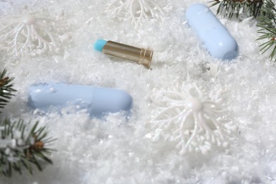 Photo of Moisturizing lip balms, Christmas decor and fir tree branches on artificial snow, closeup. Winter care