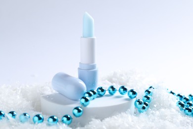 Photo of Moisturizing lip balm and Christmas decor on artificial snow, closeup. Winter care