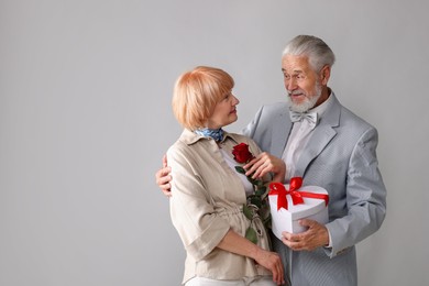 Photo of Lovely senior couple with gift box and rose on light grey background, space for text