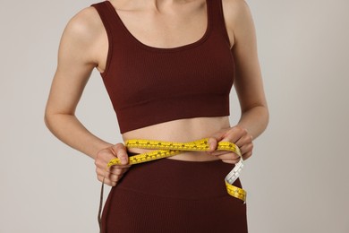 Photo of Woman measuring her belly with tape on gray background, closeup