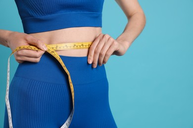 Photo of Woman measuring her belly with tape on light blue background, closeup