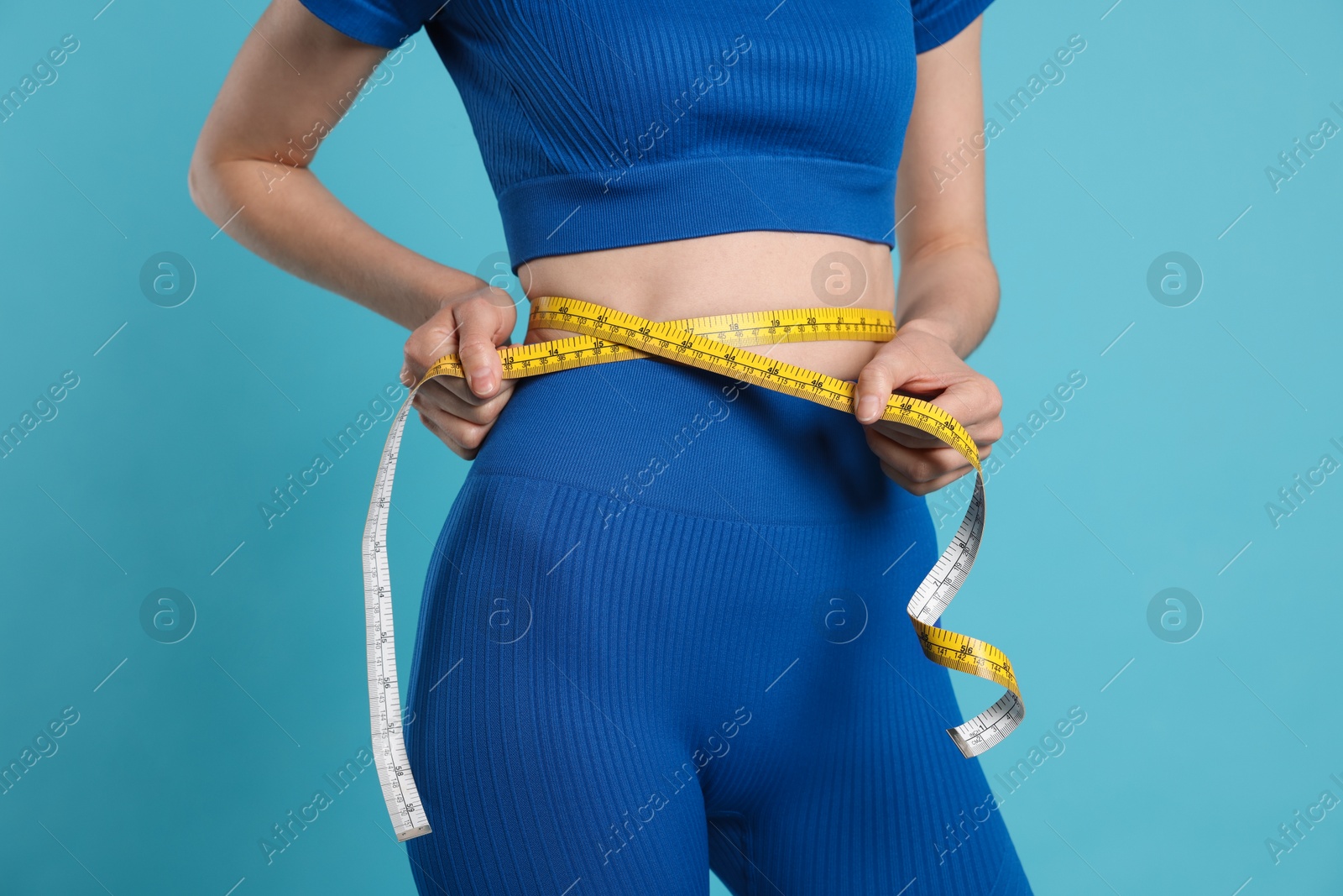 Photo of Woman measuring her belly with tape on light blue background, closeup