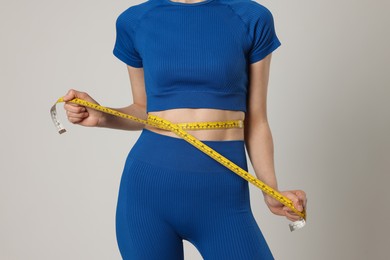 Photo of Woman measuring her belly with tape on gray background, closeup