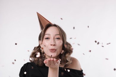 Photo of Birthday celebration. Woman with party cone blowing confetti on white background