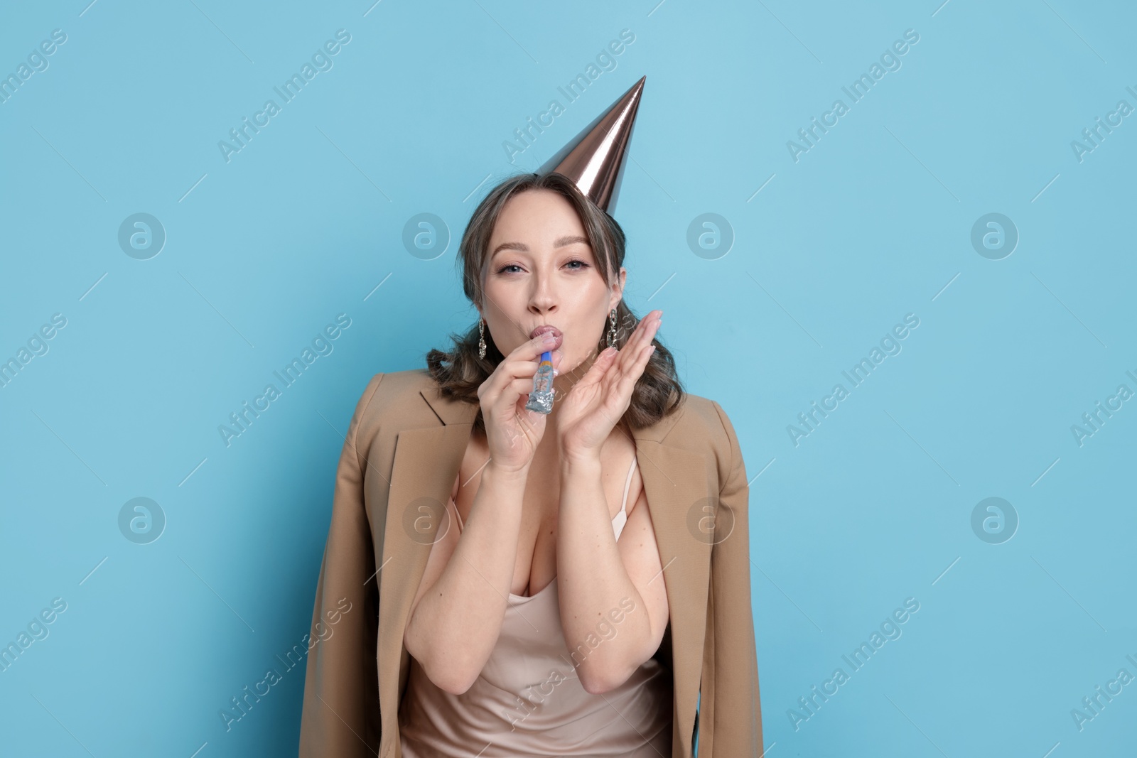 Photo of Birthday celebration. Woman with party horn on light blue background