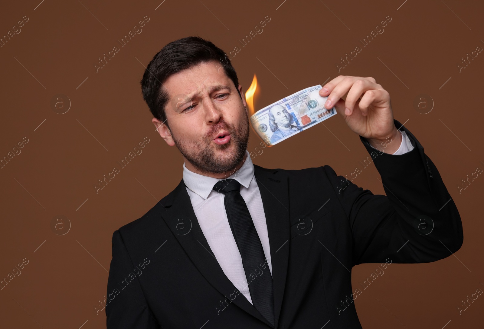 Greedy banker with burning dollar banknote on brown background Photo of Greedy banker with burning dollar banknote on brown background