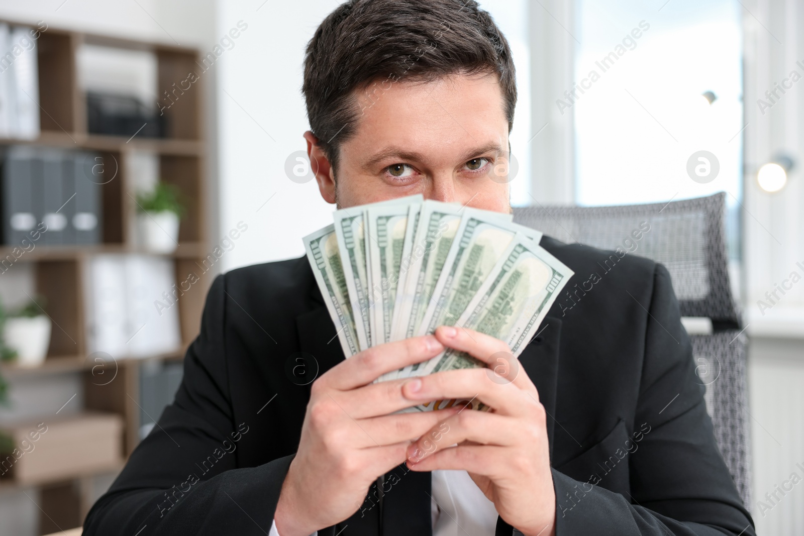 Greedy banker with dollar banknotes in office Photo of Greedy banker with dollar banknotes in office