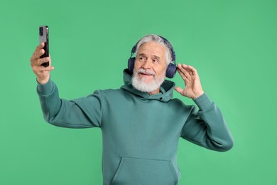 Photo of Elderly man in headphones taking selfie on green background