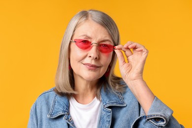 Photo of Senior woman wearing stylish sunglasses on orange background