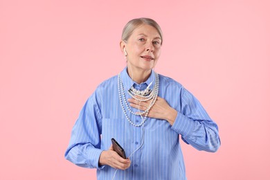 Photo of Senior woman in earphones listening to music on pink background