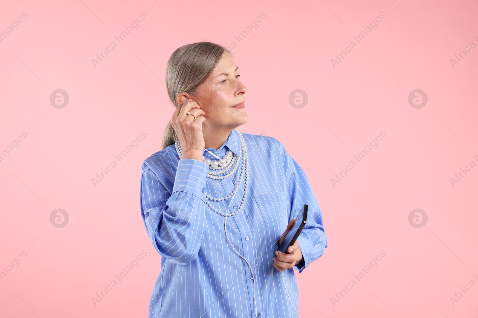 Senior woman in earphones listening to music on pink background Photo of Senior woman in earphones listening to music on pink background