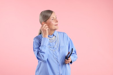 Photo of Senior woman in earphones listening to music on pink background