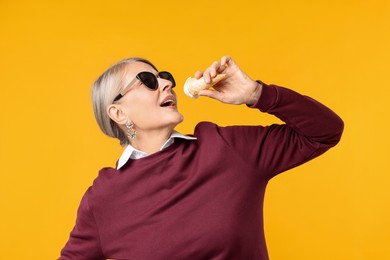 Photo of Senior woman in stylish outfit holding tasty ice cream on orange background