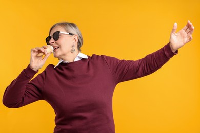 Photo of Senior woman in stylish outfit holding tasty ice cream on orange background