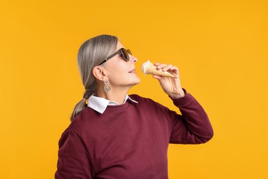 Photo of Senior woman in stylish outfit holding tasty ice cream on orange background