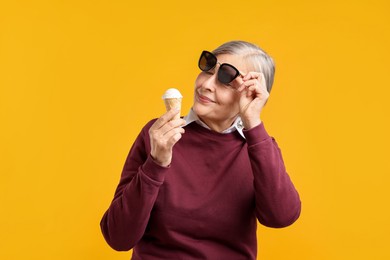 Photo of Senior woman in stylish outfit holding tasty ice cream on orange background