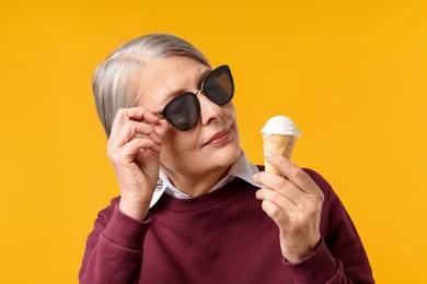 Photo of Senior woman in stylish outfit holding tasty ice cream on orange background